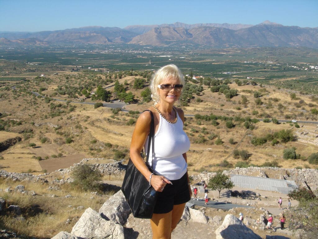 A woman standing on top of a hill with mountains in the background.