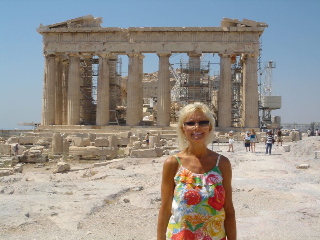 A woman standing in front of an old greek temple.