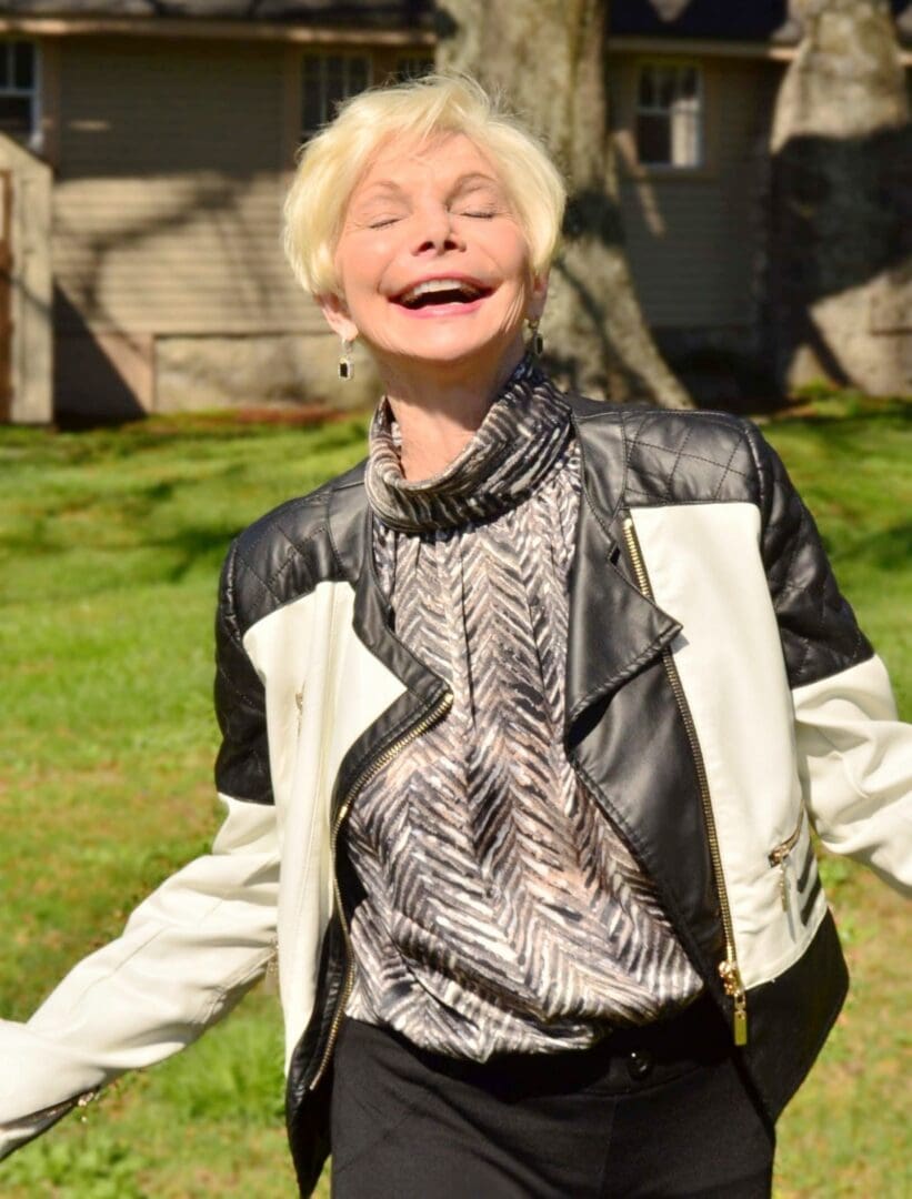 A woman in black and white jacket standing on grass.