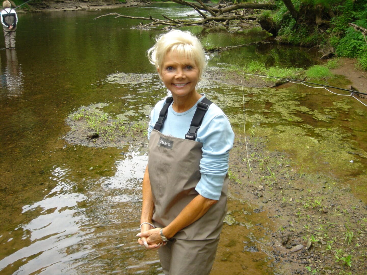 A woman standing in the water near some trees.