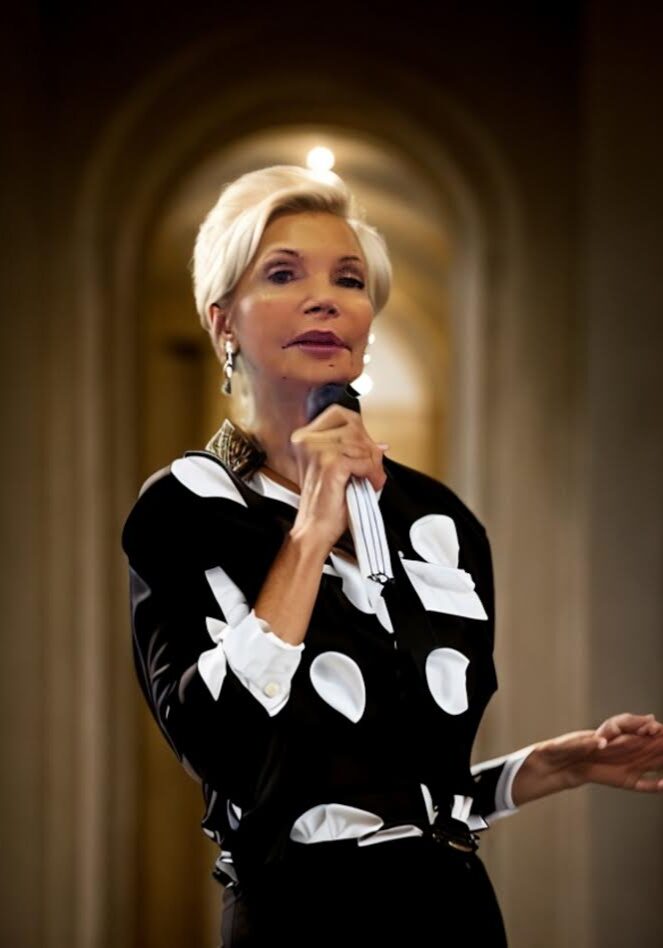 A woman in black and white polka dot jacket speaking.