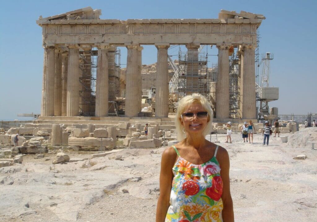 A woman standing in front of an old greek temple.