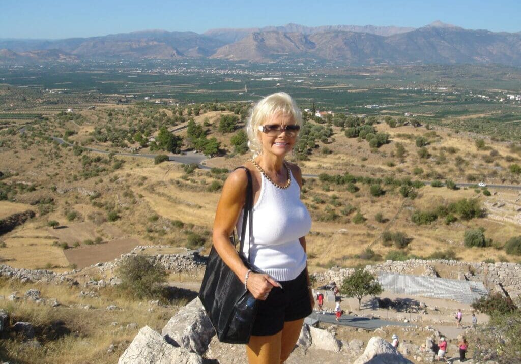 A woman standing on top of a hill with mountains in the background.